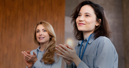 Two women smiling and applauding during a presentation or event